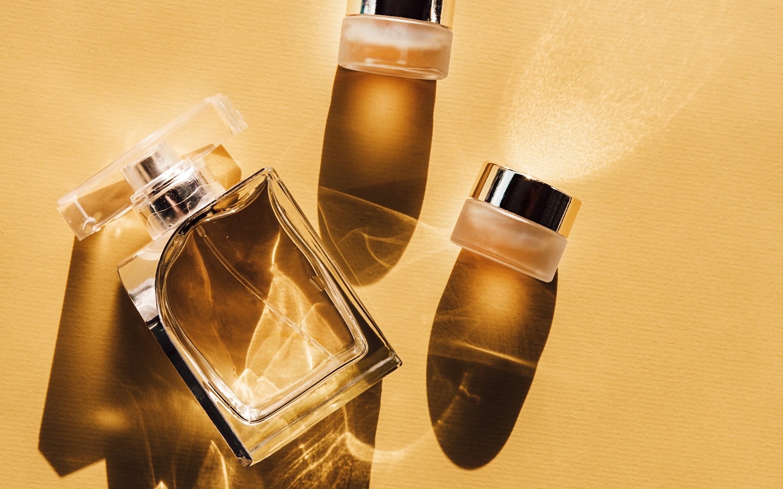 A clear perfume bottle and two cosmetic jars on a gold background